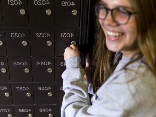 A student looks back and smiles as they put a key into a mailbox.